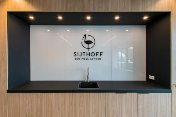 Moderne kitchenette met zwart werkblad en het logo van Sijthoff Business Center op een glanzende witte achterwand.